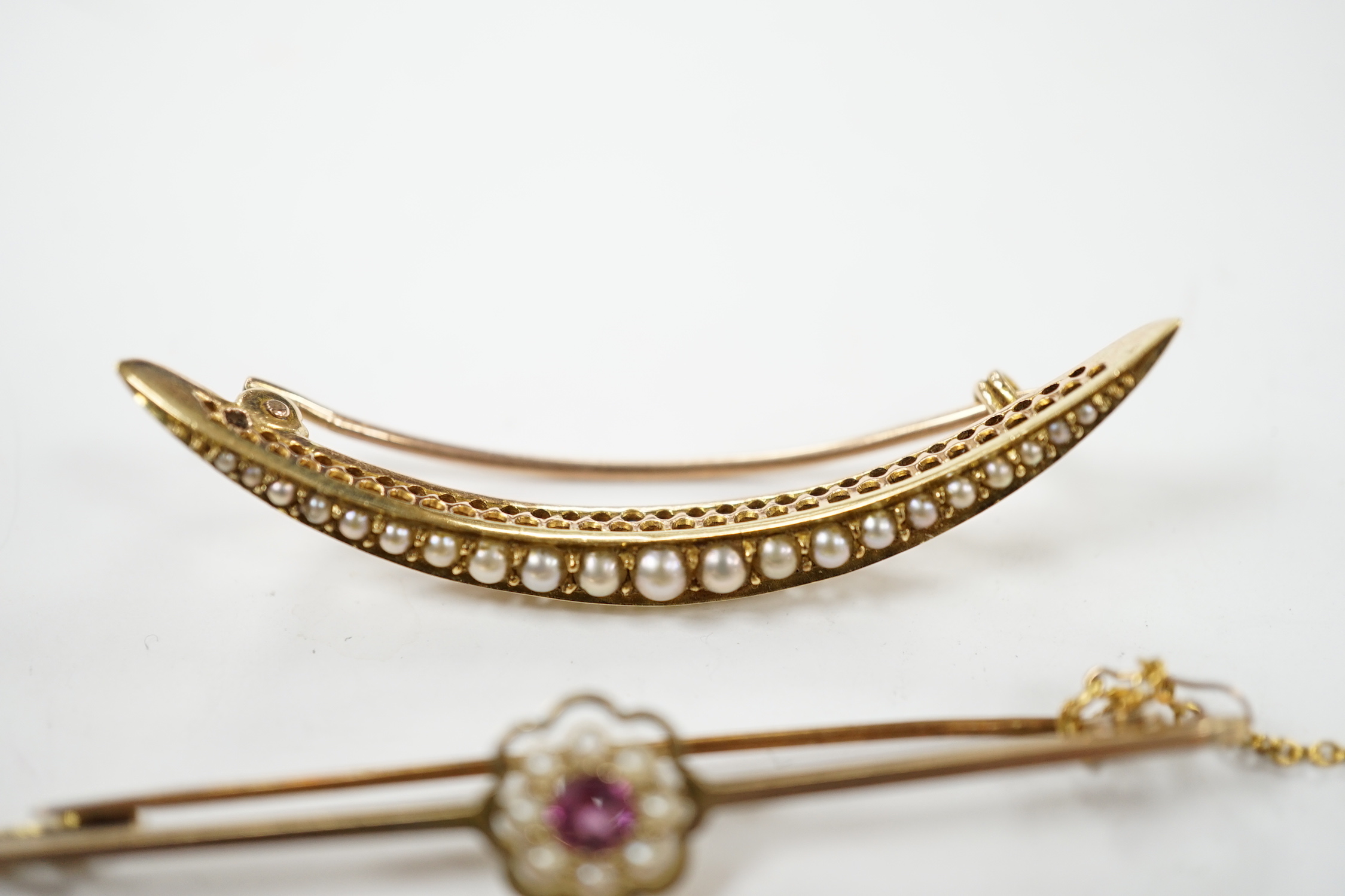 An Edwardian 15ct, ruby and diamond chip set three stone bar brooch, 45mm, a 9ct and gem set bar brooch and a yellow metal and seed pearl set crescent brooch.